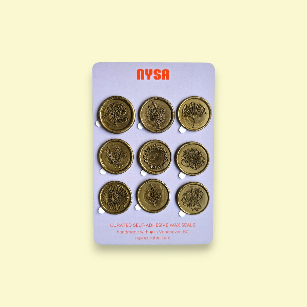 A photo of the Botanical collection and packaging. The 9 wax seals are mounted on a lilac backing that has the NYSA branding in orange. The photo is on a light yellow background. The seals from top left to right depict: a hydrangea, a fresh bouquet, a ginko leaf, rosemary twigs, a wreath, a peony, a daisy, a branch, and a flower stem.
