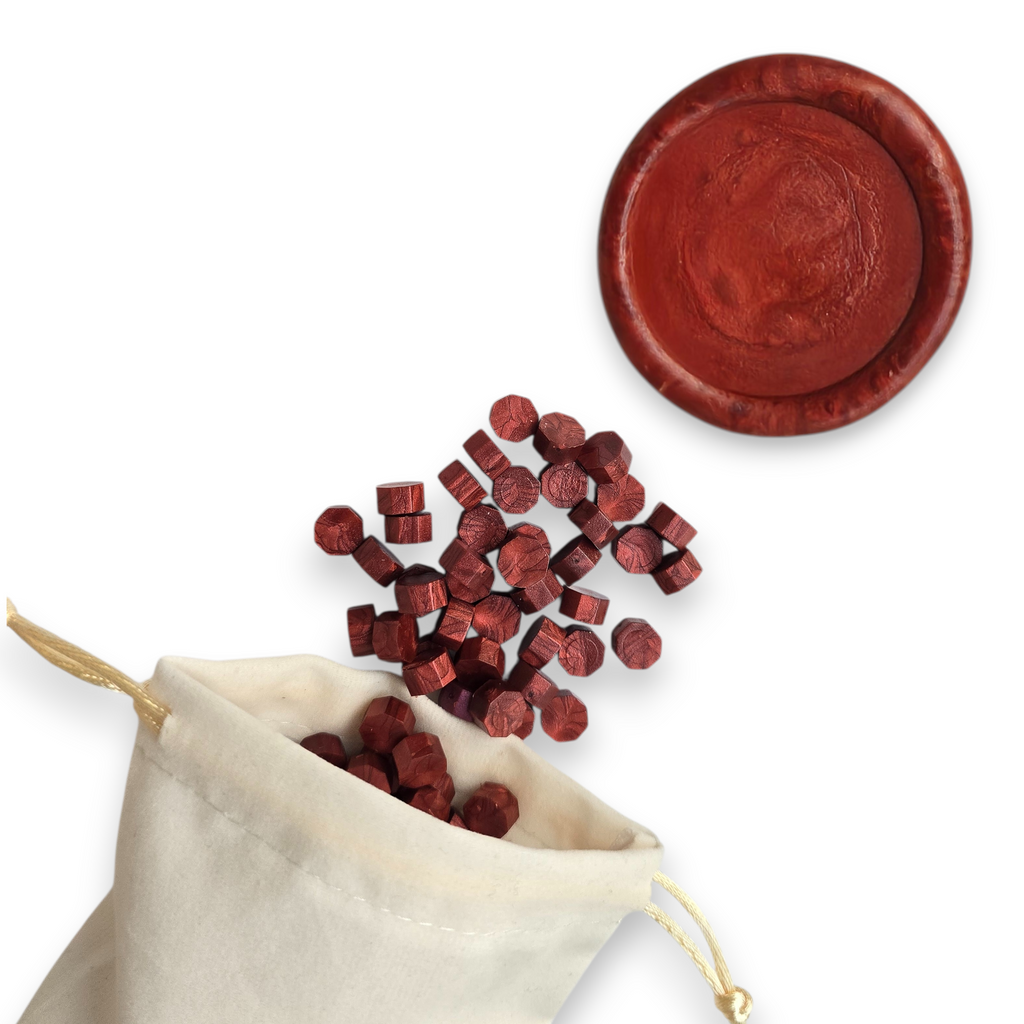 Ruby wax beads spilling out of a beige drawstring bag onto a white background. In the top right corner is a blank wax seal in the showcasing the ruby colour option.