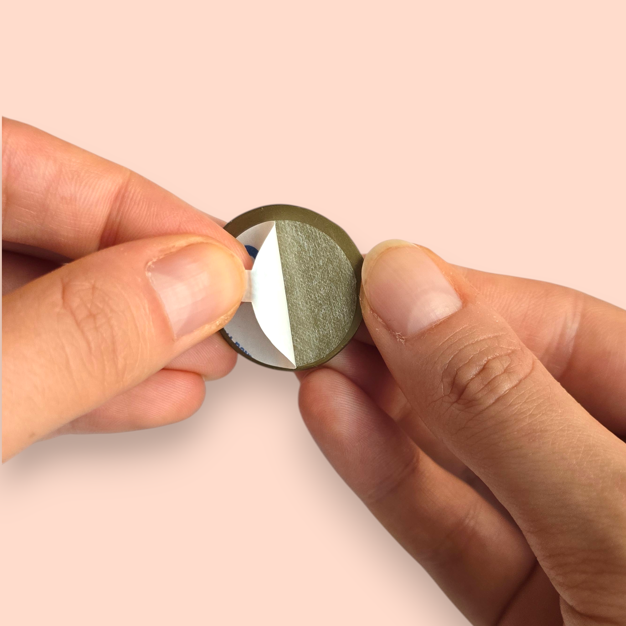 Hands holding a wax seal as the adhesive backing is peeled off against a light orange background